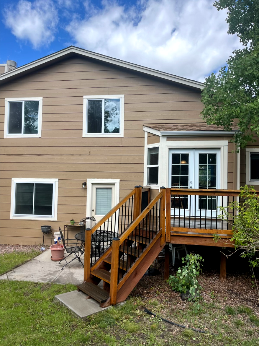 Tan house with a deck and stairs. Windows and a door are visible. Brown horizontal lines on the siding.