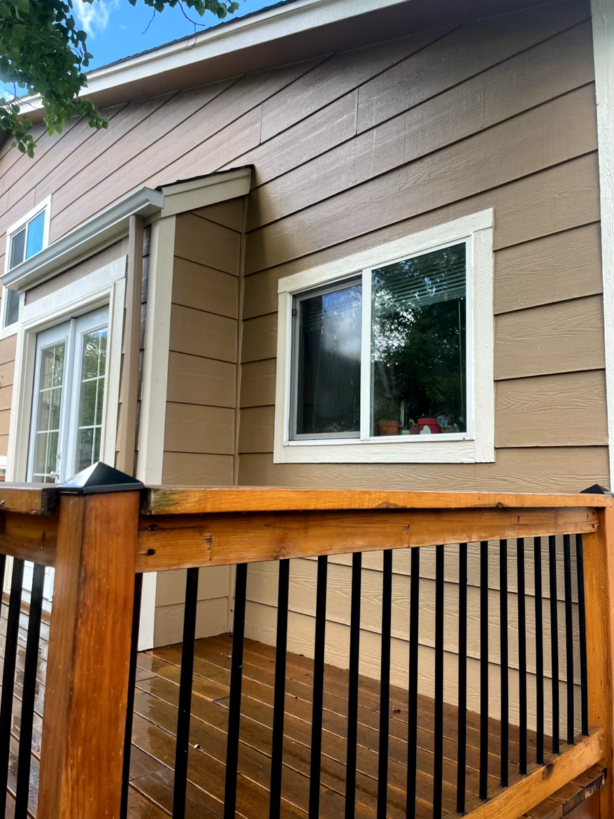 Wooden deck with black railings in front of a tan house with white-framed windows.