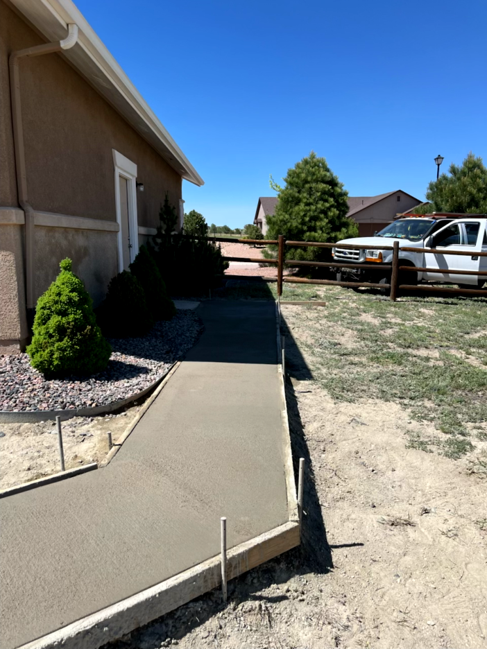 Freshly poured concrete sidewalk next to a house under a clear, blue sky.