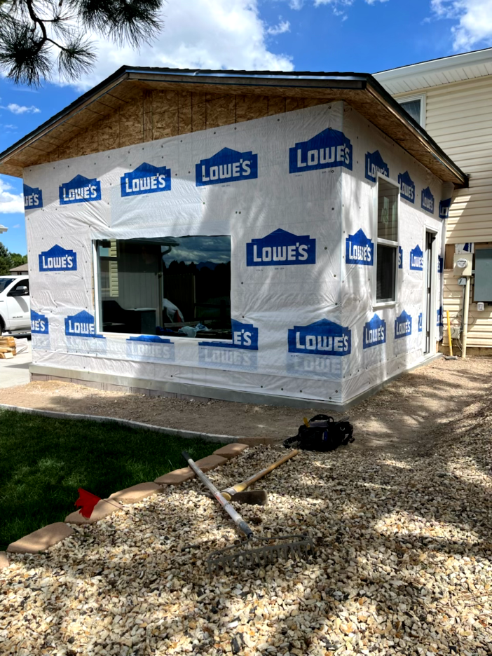 Construction of a house addition with blue and white wrap, windows, and exposed wood roof.