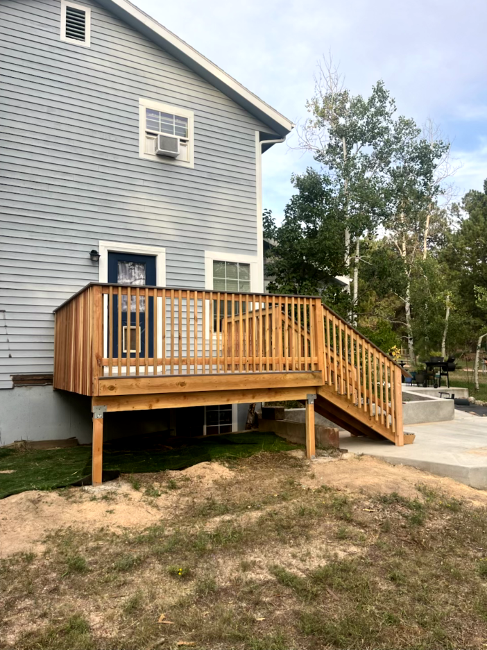 Wooden deck with stairs attached to a blue house, set in a grassy backyard.