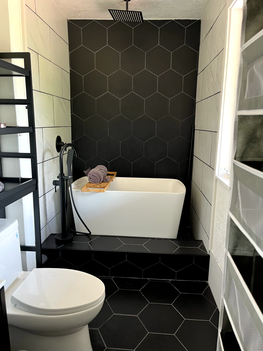 Bathroom with black hexagon tile, white tub, and toilet.