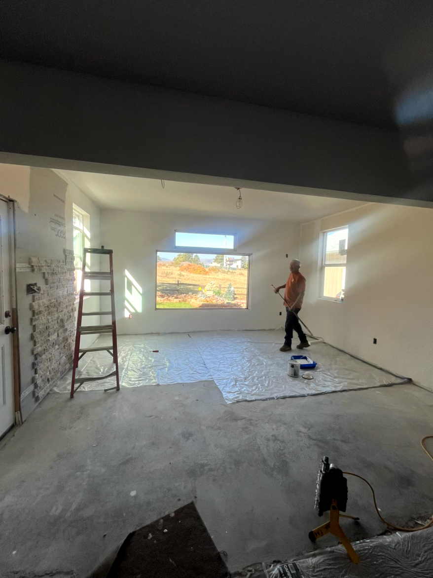 Construction worker in a room, applying flooring. Light projected on wall; ladder, open doorway.
