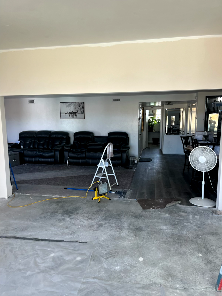 Interior view of a room with black sofas, a step ladder, and a fan. Other rooms are visible through doorways.
