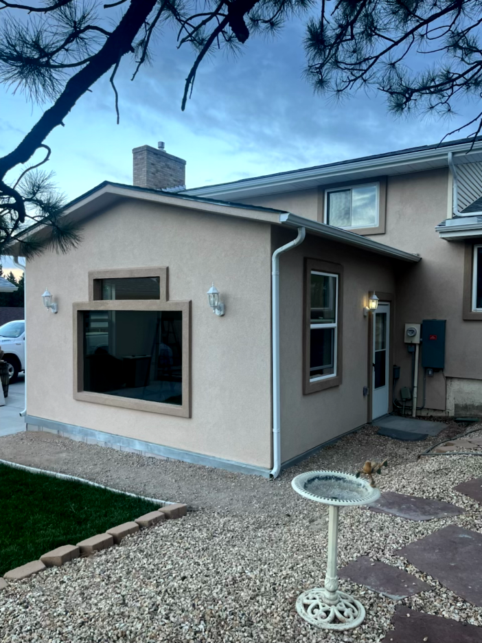 Exterior of a light-colored stucco house addition with windows, a door, and gravel landscaping.