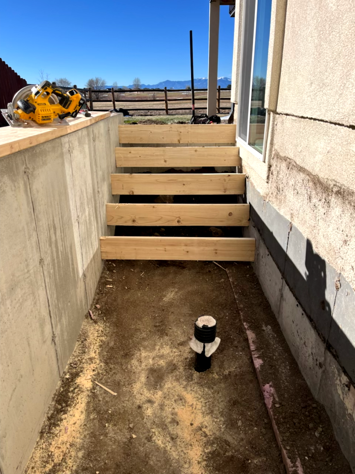 Wooden stairs under construction next to a building, with a cement wall on one side.
