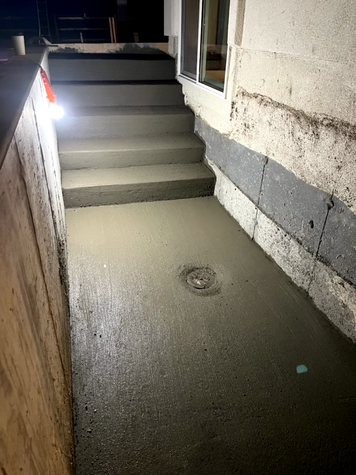 Newly poured concrete steps and landing beside a building foundation; lit by a work light.