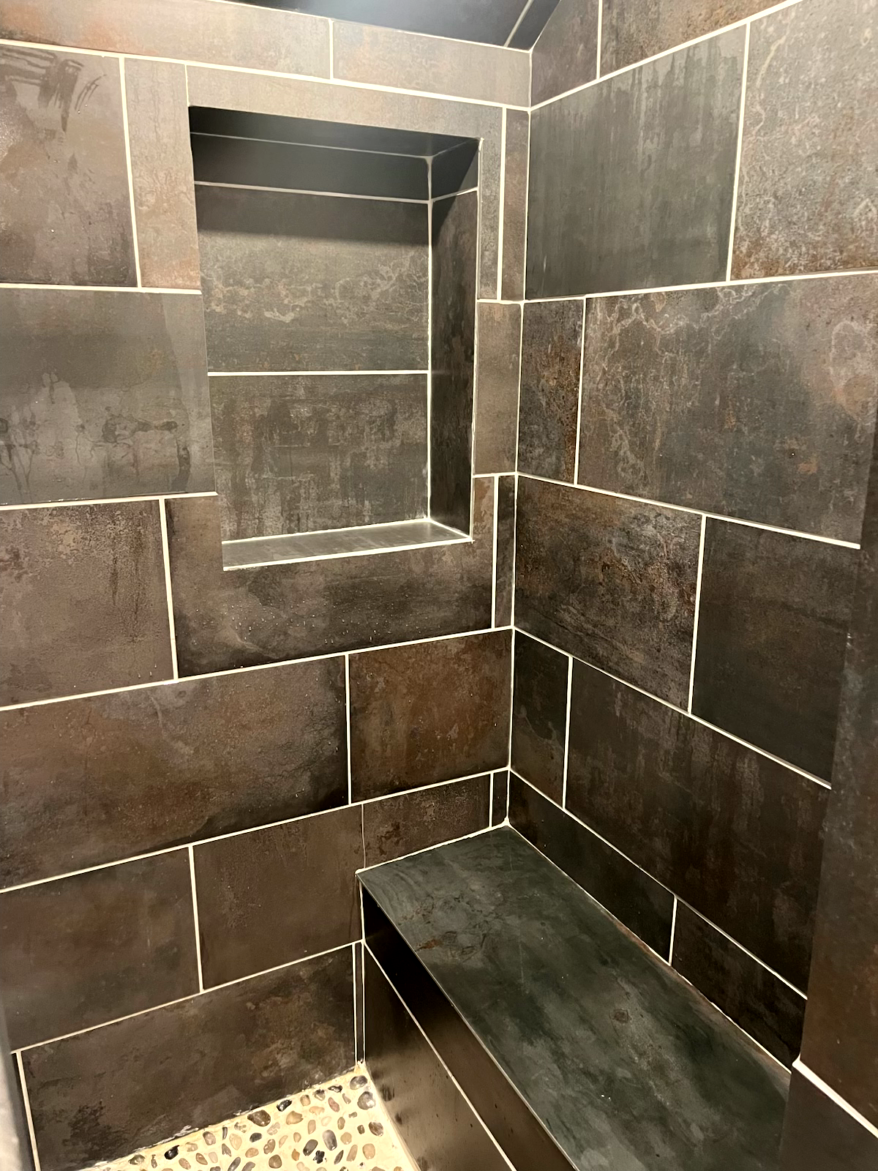 Dark brown tiled shower with built-in bench and recessed shelf.