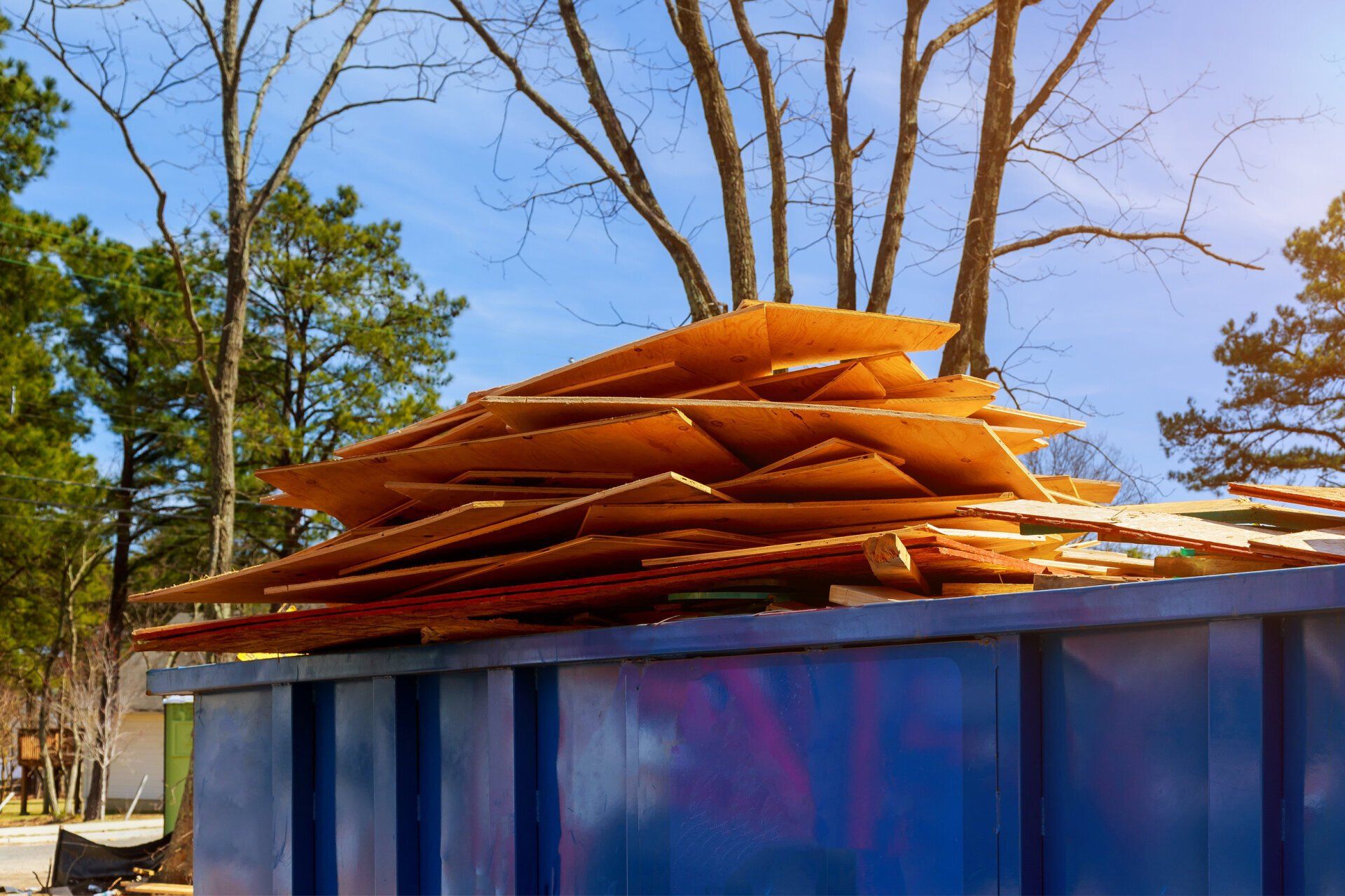 A blue dumpster filled with a pile of wood.
