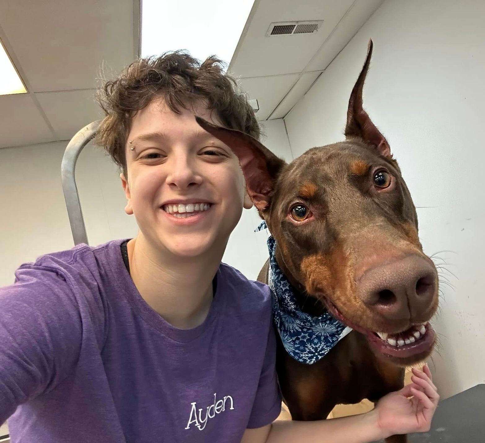 A man wearing a purple shirt with the word aurien on it poses with a brown dog