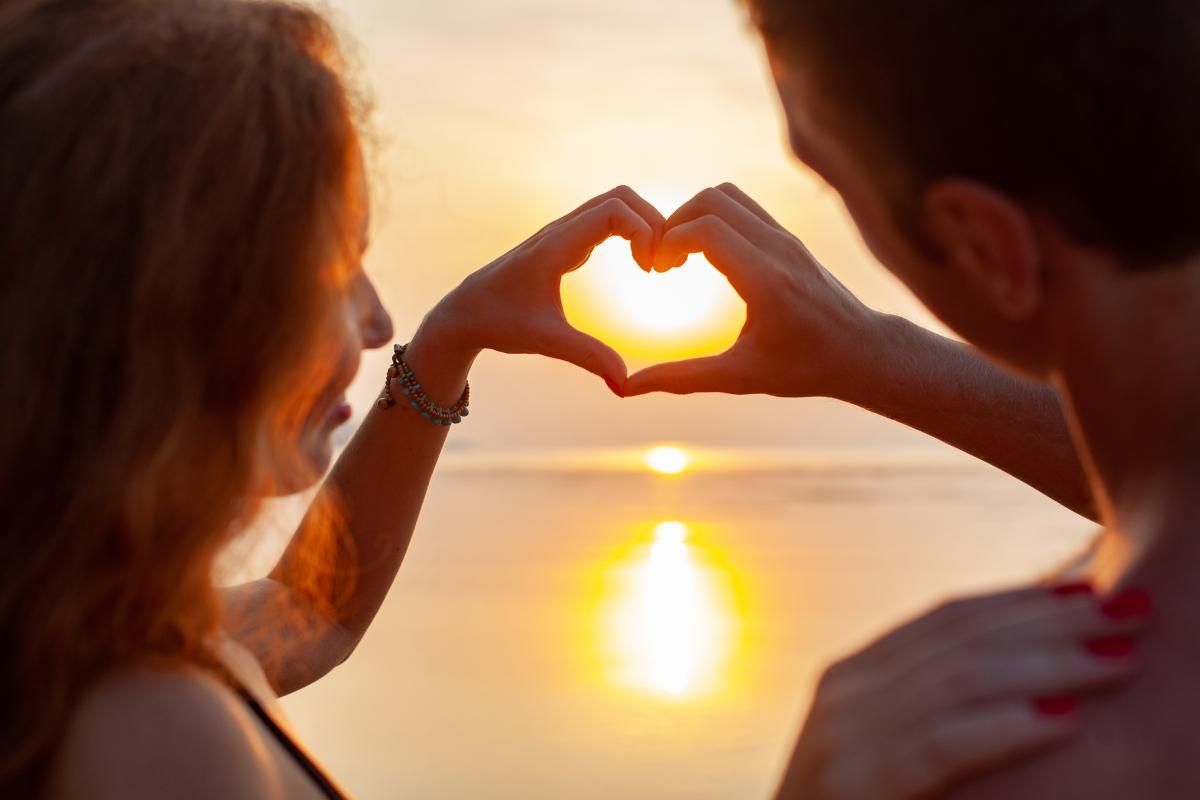 Imagem de um casal fazendo coração no pôr do sol, ilustrando uma viagem de Lua de Mel em Morro de São Paulo.