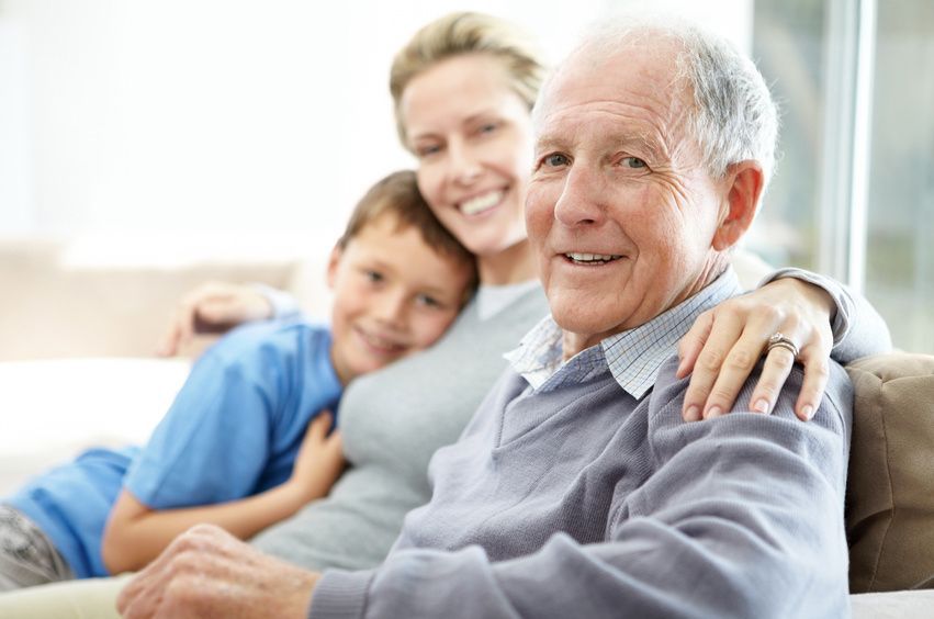 Familie bestehend aus Großvater, Tochter und Enkelsohn sitzt auf brauner Couch.