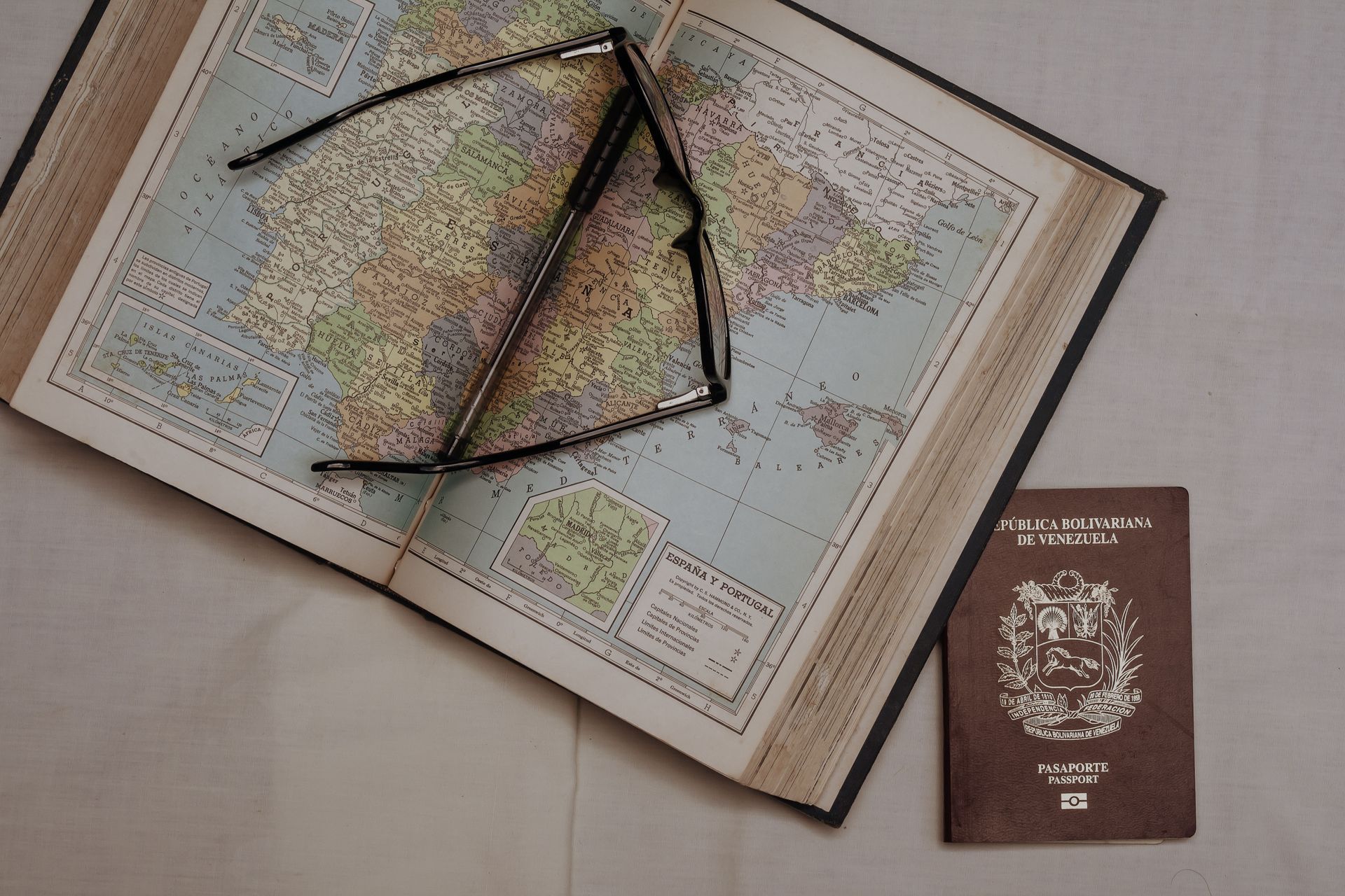 Open map with compass and pencil, next to a brown passport on a table.