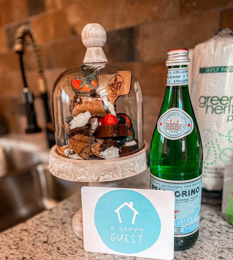 A bottle of water is sitting on a counter next to a cake stand for nice presentation when guests arrive to their rental.