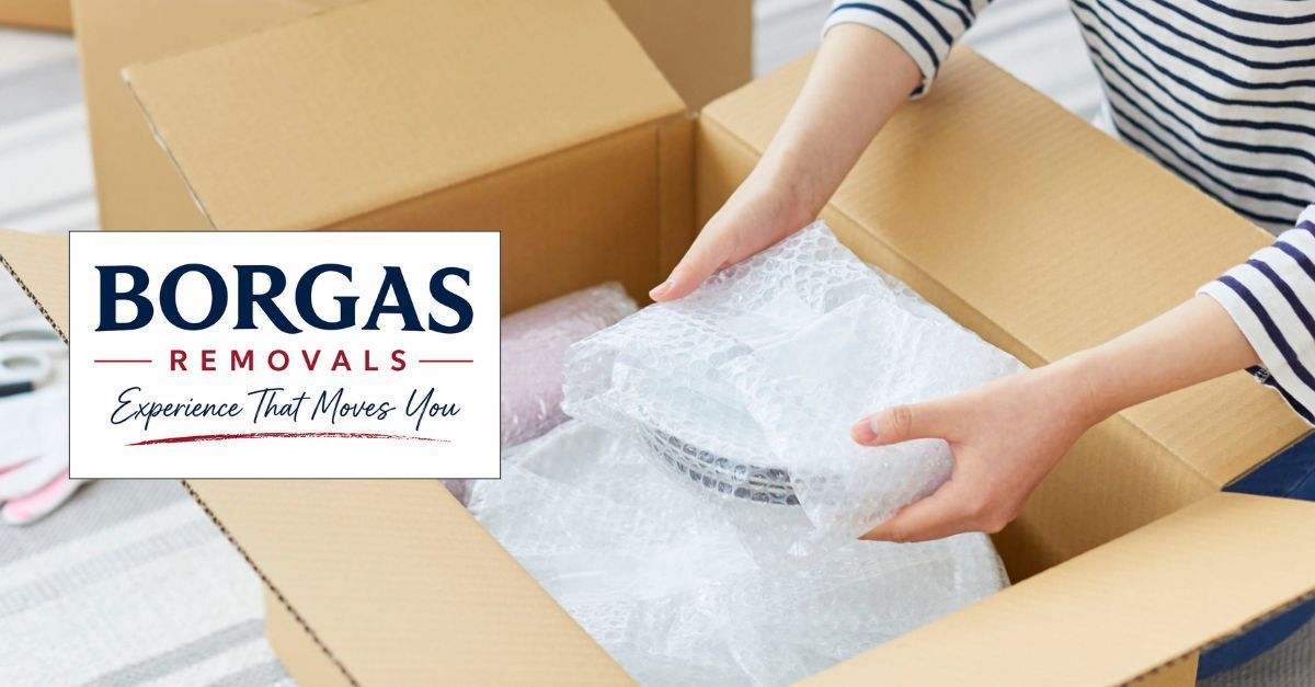 Person packing fragile household items in bubble wrap into a moving box, with Borgas Removals brand.