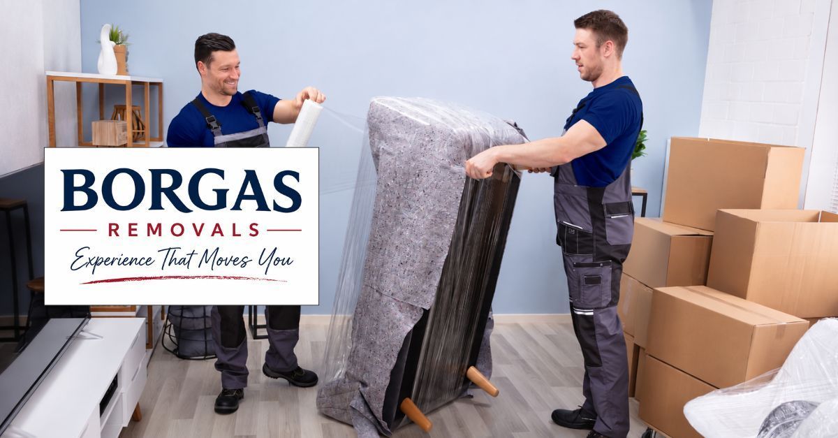 Two professional removalists wrapping household furniture with protective moving materials.