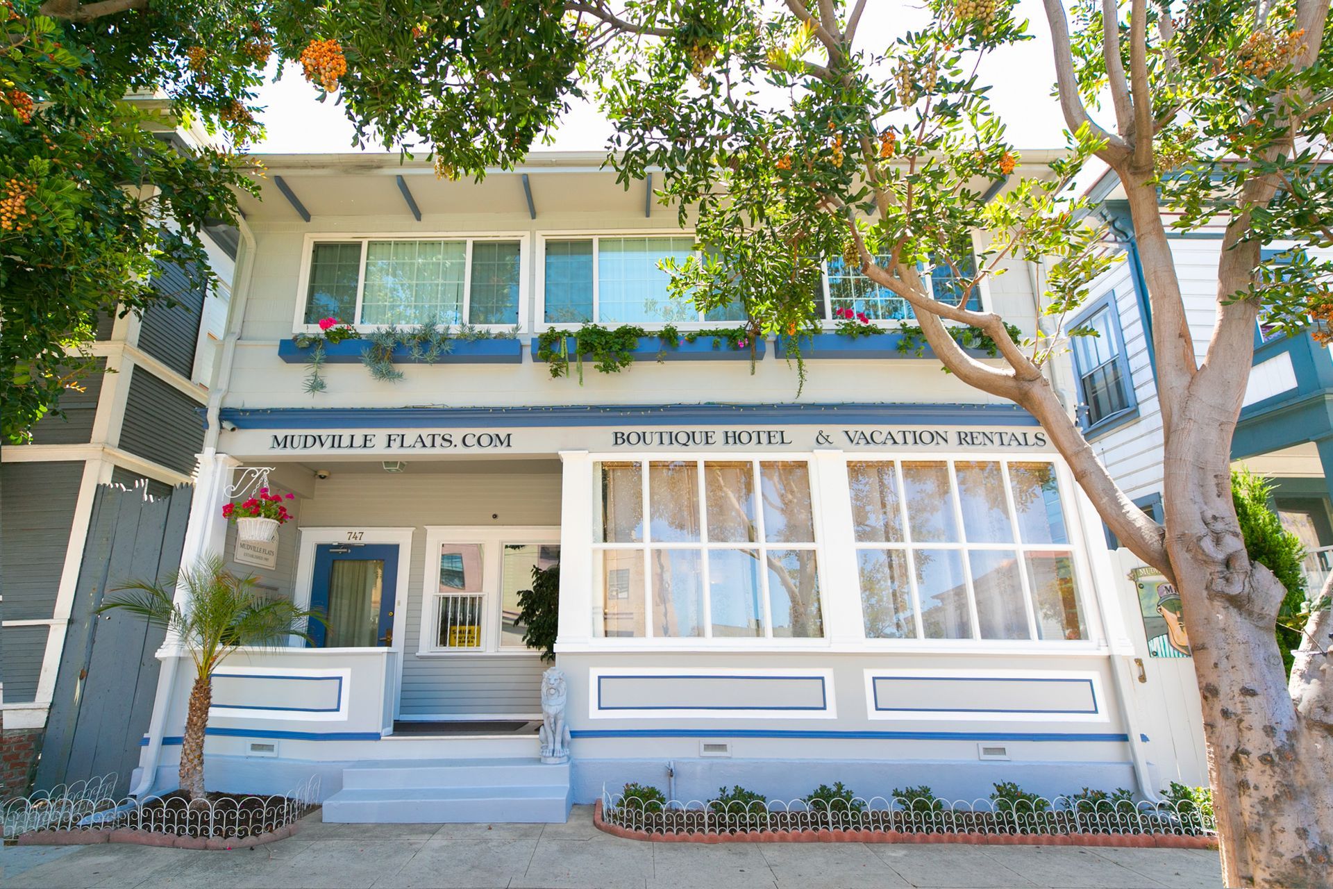 Two-story boutique hotel and vacation rental building with light gray siding, blue trim, and large windows.