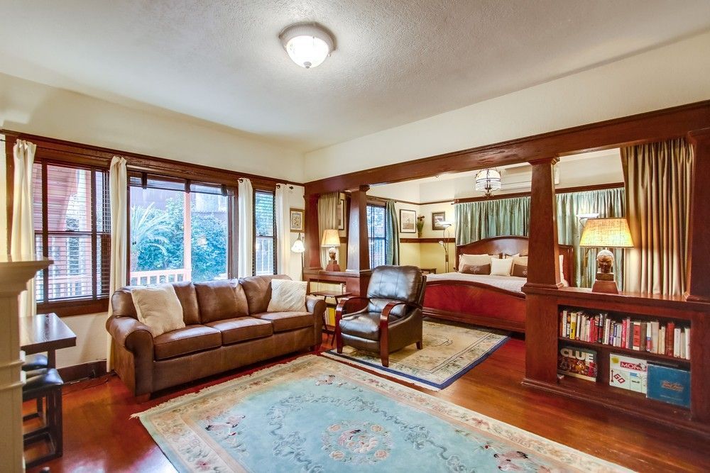 A cozy living and bedroom area with a brown leather sofa, a recliner, a bed, and built-in bookshelves in a wood-trimmed room.