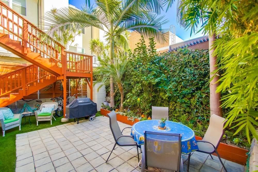 An outdoor patio area features a small round table with chairs, a grill, and a wooden staircase against a white building.