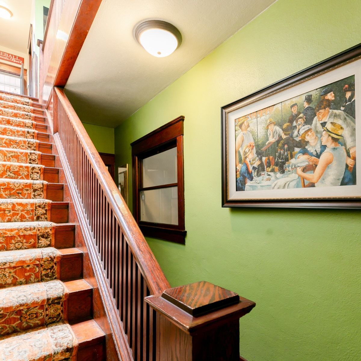 Stairs with a patterned orange runner, a wooden banister, and a framed painting on a lime green wall.