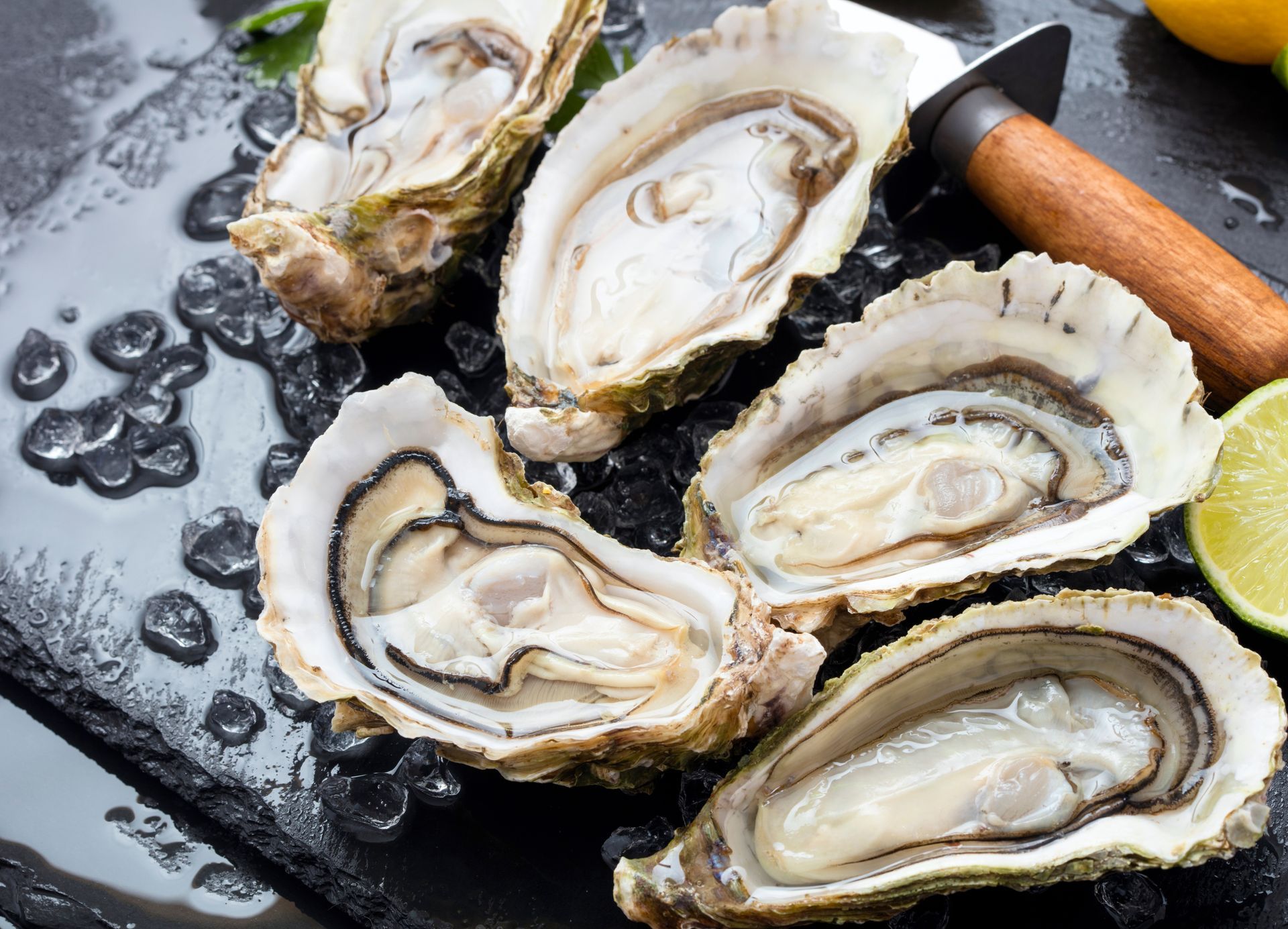 Fresh oysters on the half shell served on ice, accompanied by a lime wedge and an oyster knife.