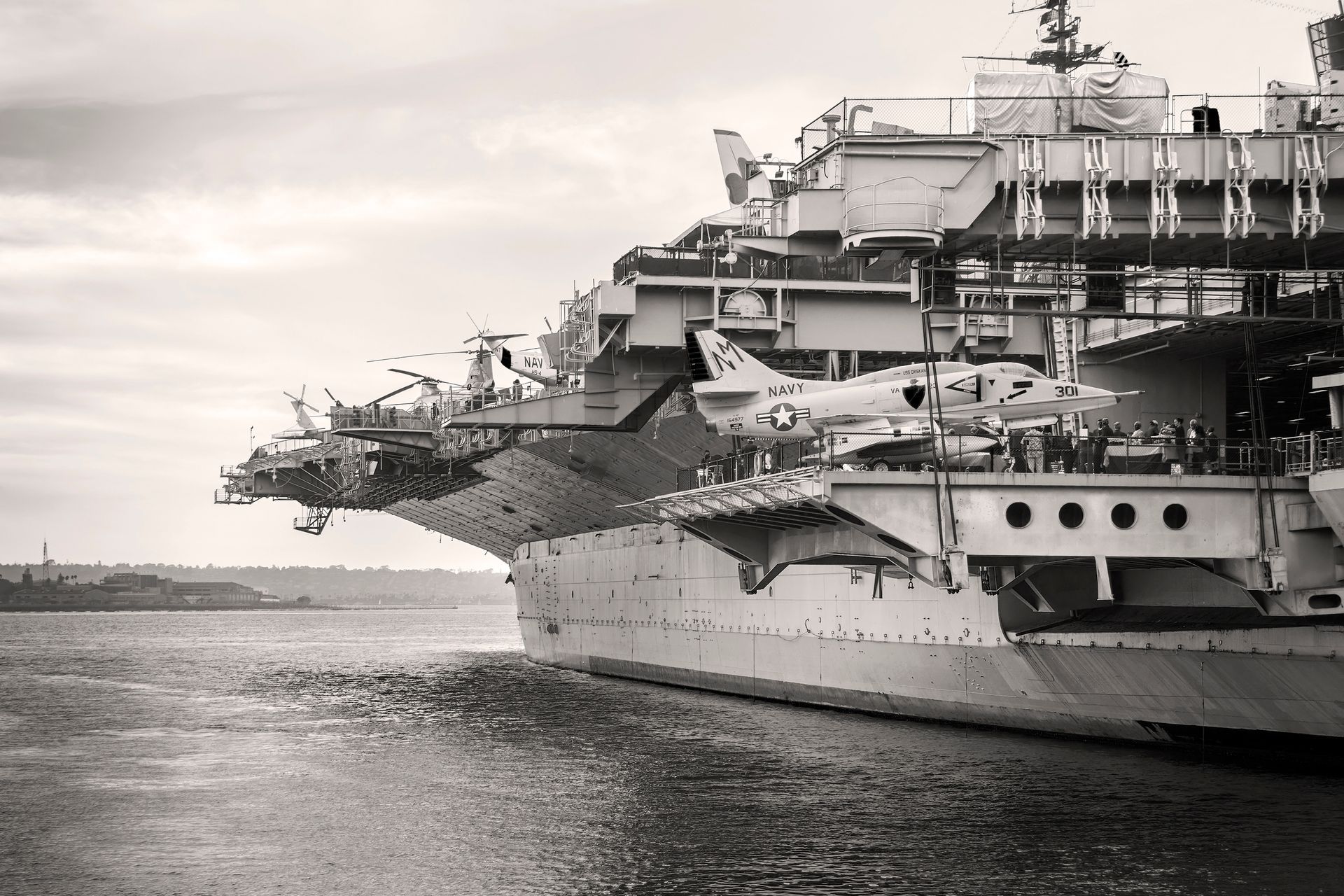 A black-and-white view of a US Navy aircraft carrier with fighter jets parked on its flight deck.