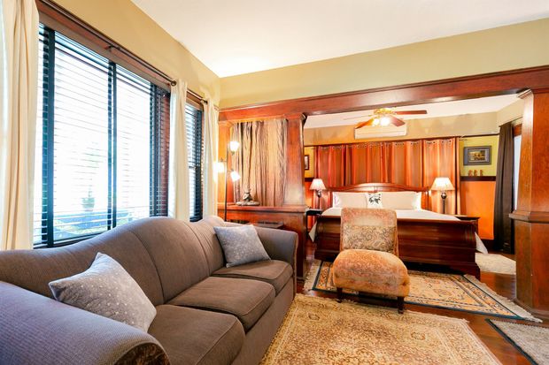 A cozy living space featuring a gray sofa in the foreground, leading to a bedroom with a large bed and wood paneling.