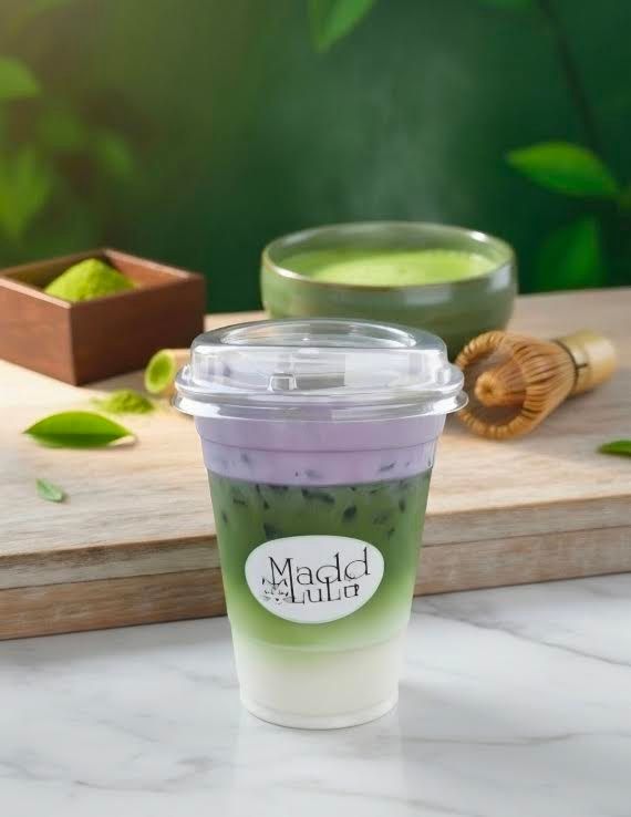 Purple and green layered drink in a clear cup on a table with mint leaves and a rolling pin nearby
