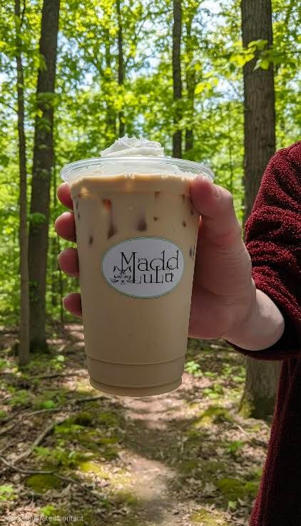 Hand holding a whipped-cream iced coffee in a forest trail setting