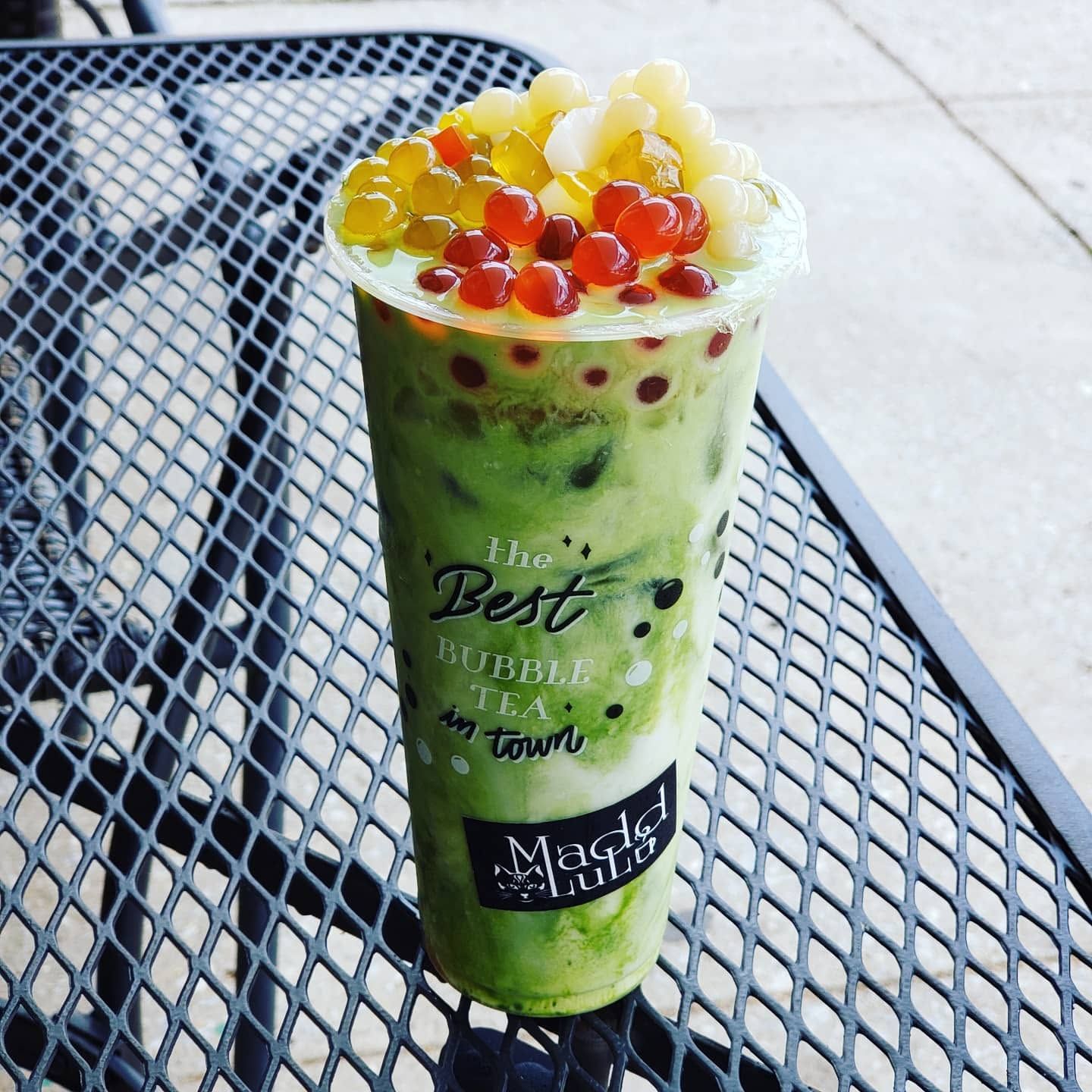 Green bubble tea topped with colorful jelly on a metal café table