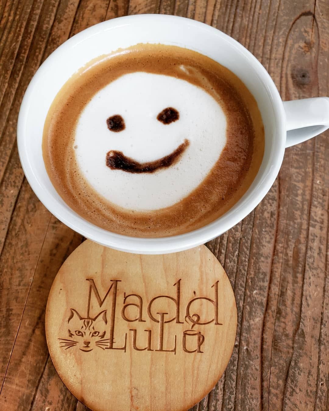 Smiling latte art in a white cup on a wooden table with a carved wooden coaster