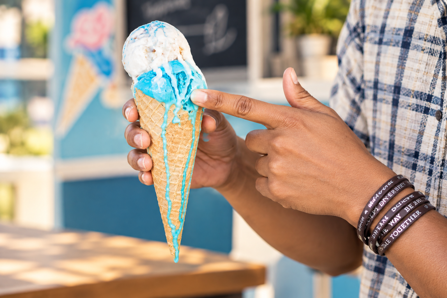 Hand holding a blue ice cream cone, with a finger pointing at it in front of a shop counter
