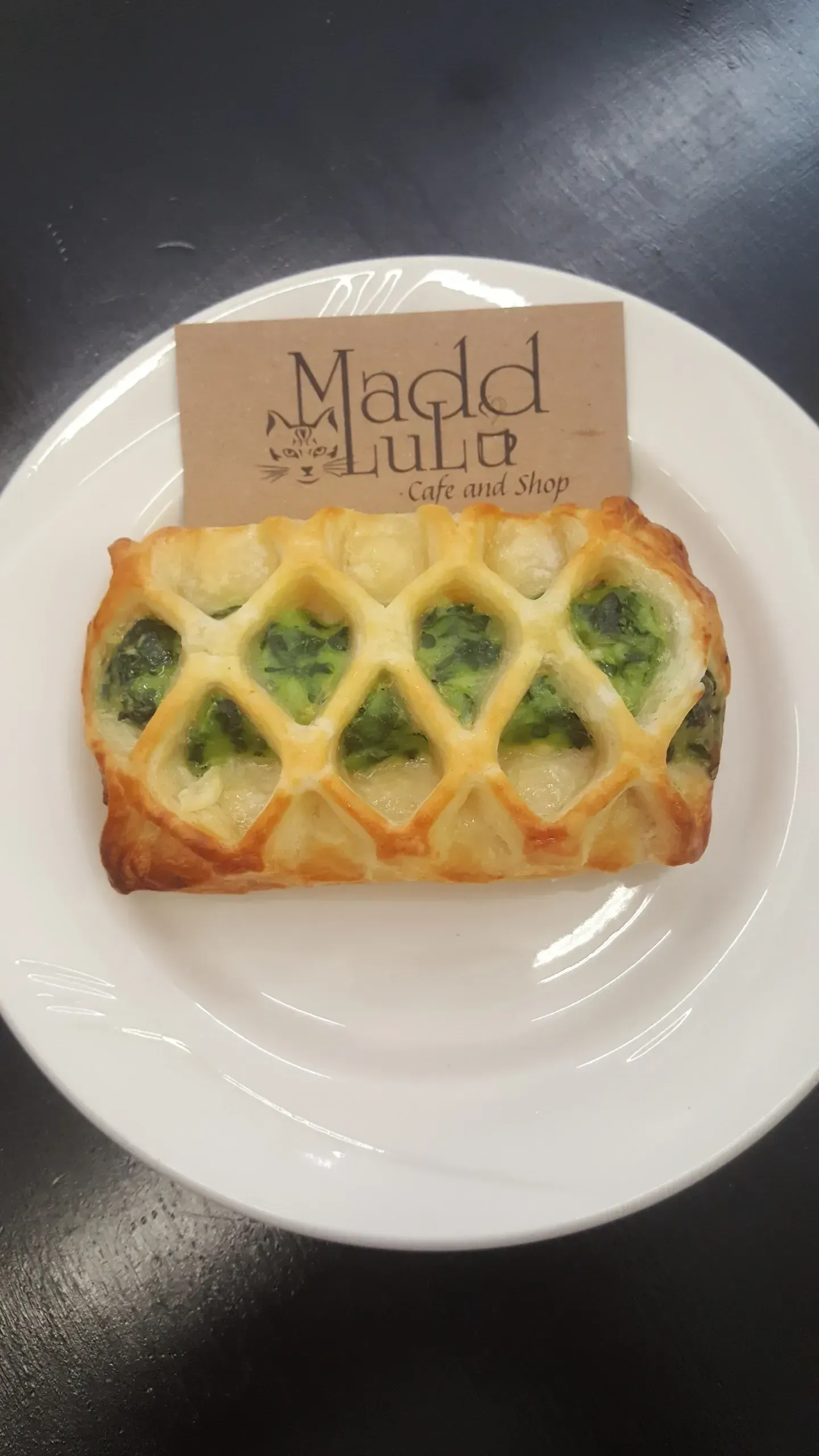 Baked pastry with green filling on a white plate with a logo on a dark table.
