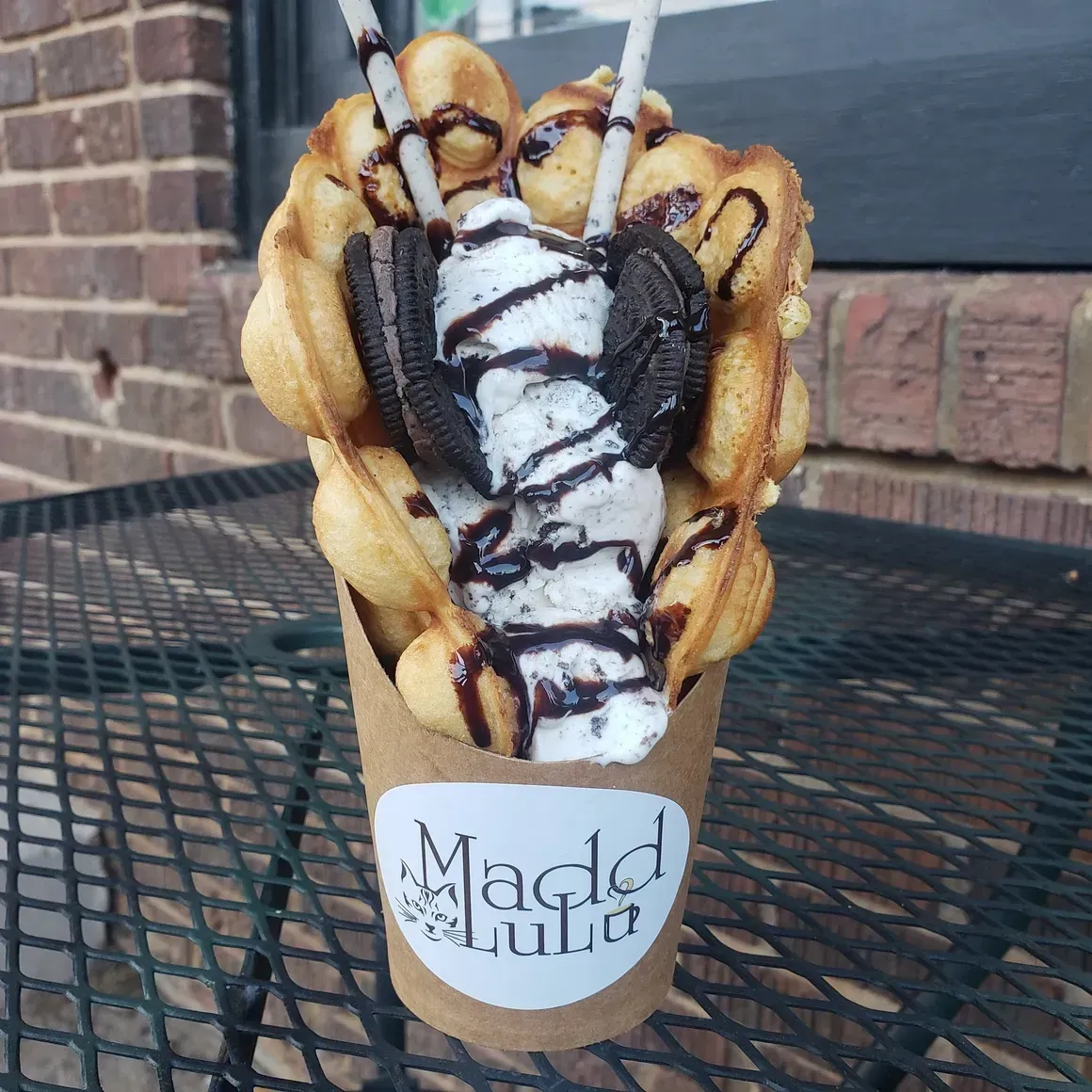 A waffle cone dessert topped with ice cream, whipped cream, and chocolate drizzle in a branded cup holder
