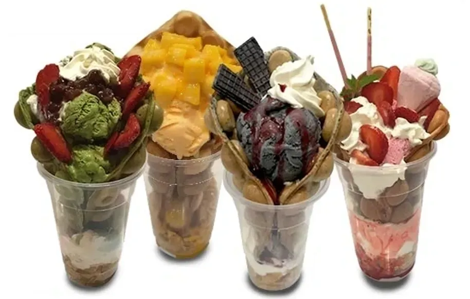 Four colorful fruit and whipped cream parfaits in clear cups, topped with mango, berries, and chocolate wafers