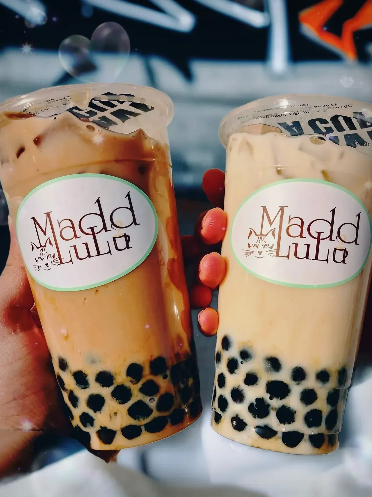 Two iced milk teas with black tapioca pearls and Madd adda logos held in hand