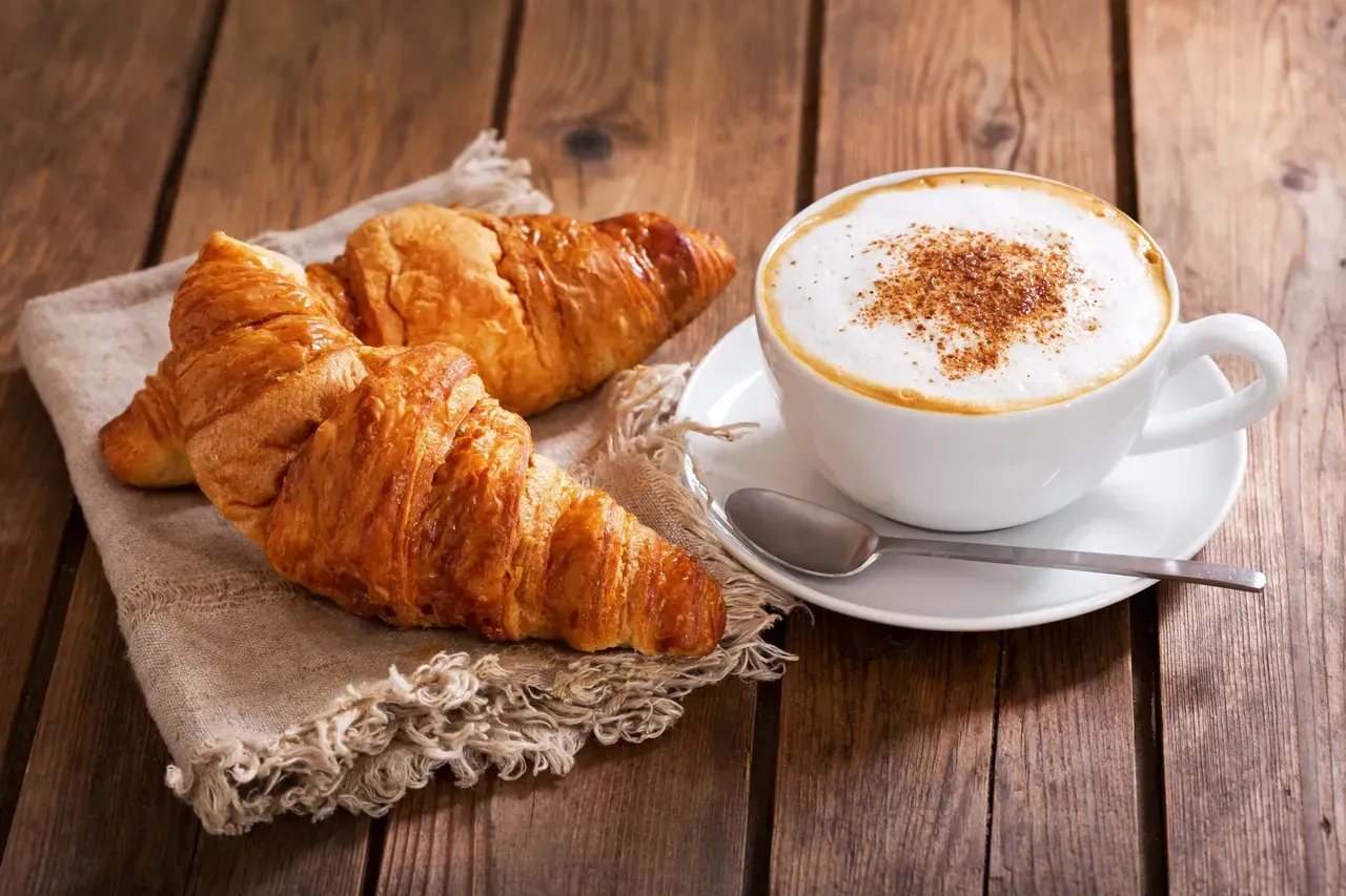 Croissants and a cappuccino on a rustic wooden table with a spoon and napkin