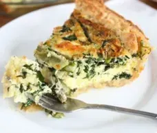 Slice of spinach quiche on a white plate with a forkful taken out