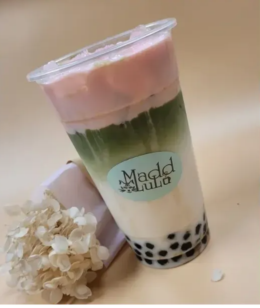 Layered pastel bubble tea with black tapioca pearls and a flower beside it on a beige background