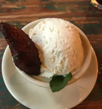 Vanilla ice cream scoop in a white bowl with a dark caramelized garnish on a saucer.
