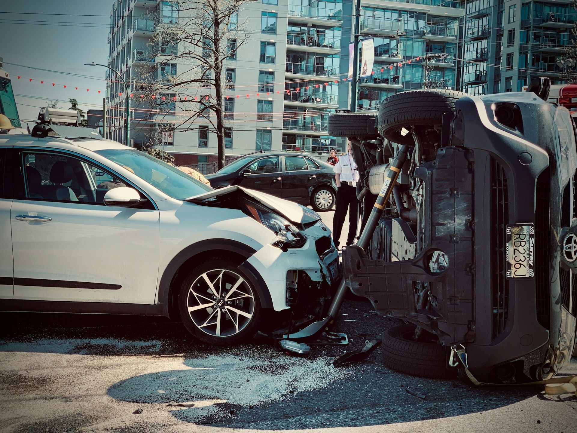 Car accident scene: white SUV with front-end damage, black SUV flipped over, shards of glass on the street.