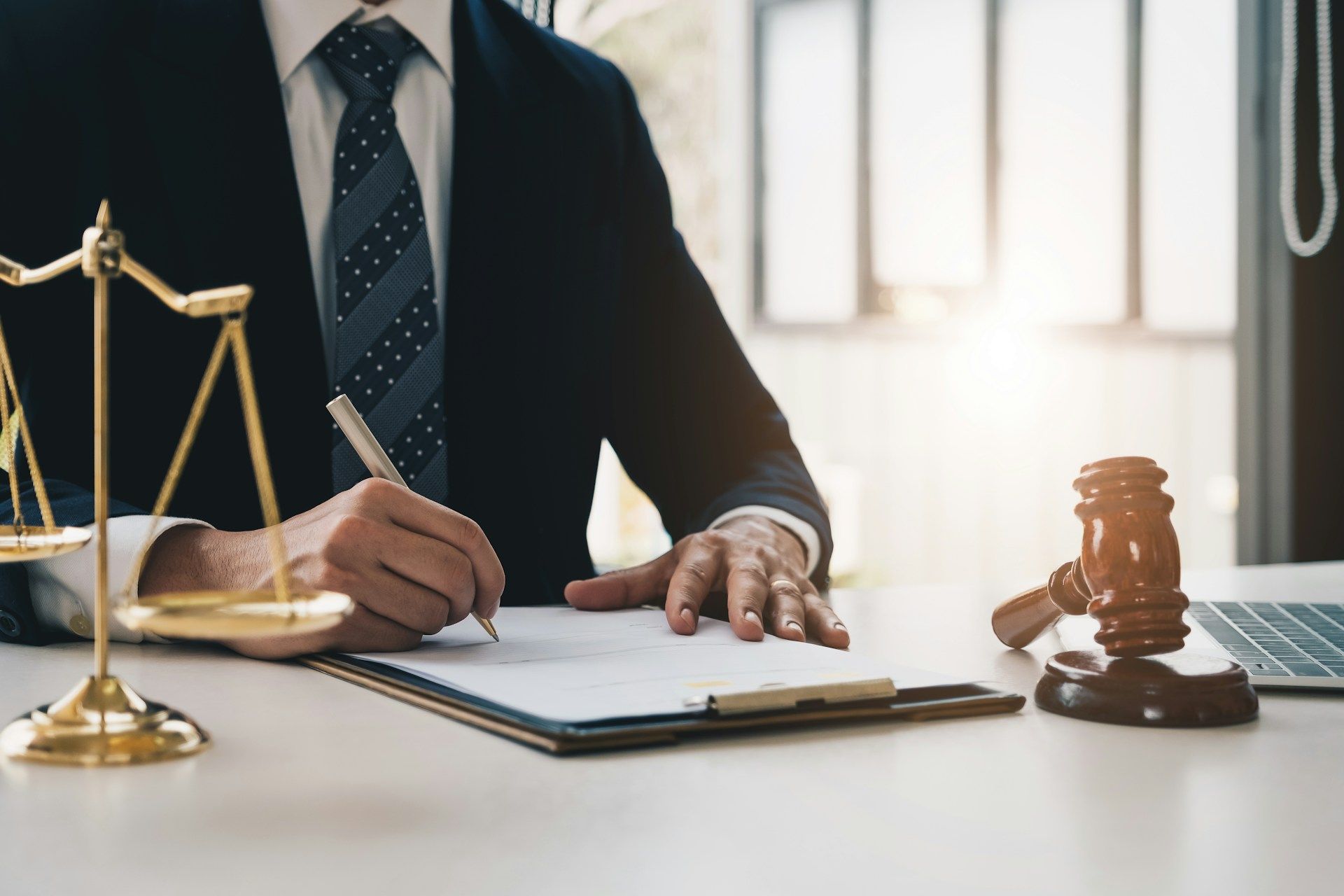 Lawyer in suit writing at a desk, scales of justice and gavel nearby.