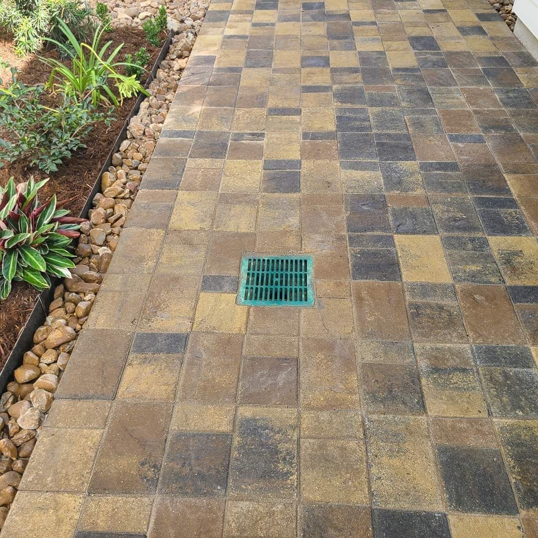Brick patio with drain, bordered by a garden and rocks.