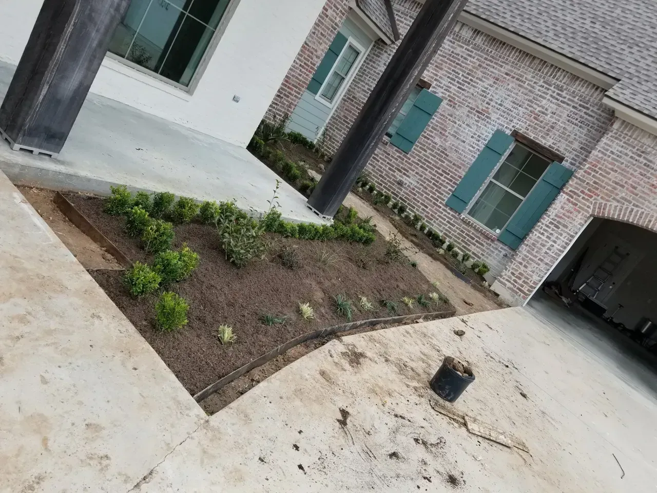 Exterior view of house with brick walls, green shutters, and freshly planted garden beds with shrubs.