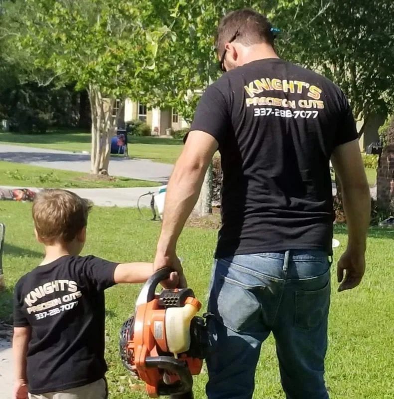 Man and child holding a leaf blower on a lawn; both wearing black shirts with 