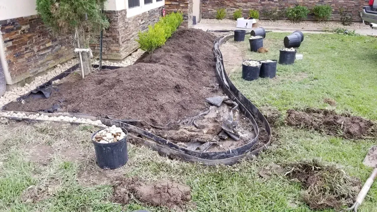 Garden bed with mulch, border, and pots; lawn in front of house.