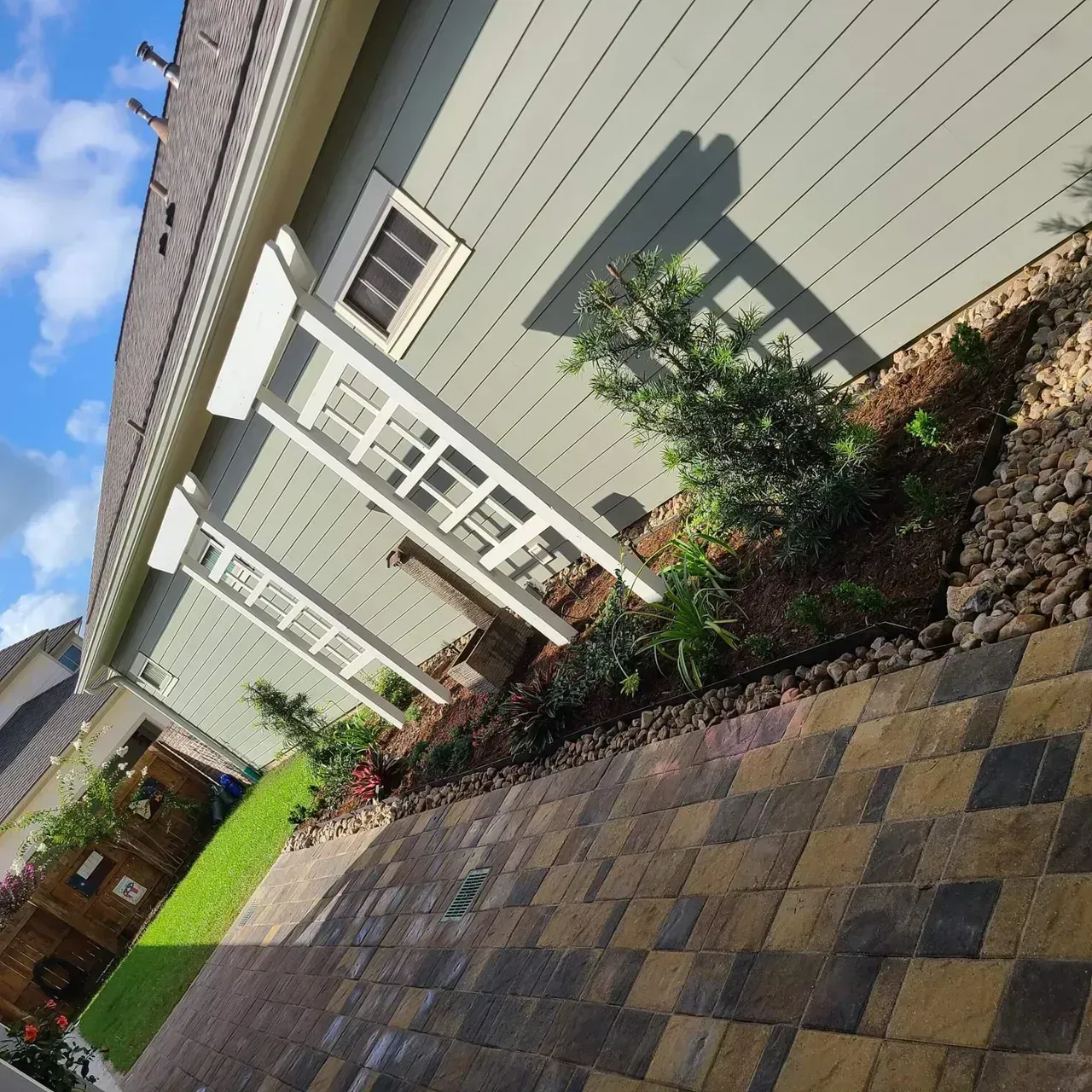 Landscaped house exterior with stone patio, flower bed, and blue siding.