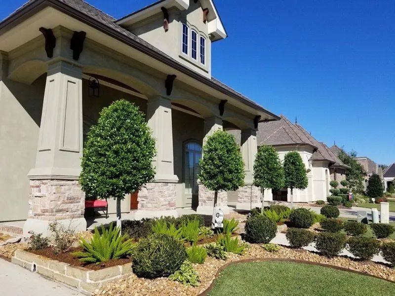 Stone and stucco house with manicured lawn and trees under a clear blue sky.