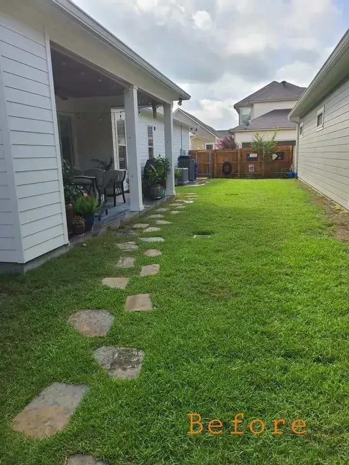 Backyard with stepping stones leading to a grassy area, flanked by a house and a fence, cloudy sky.