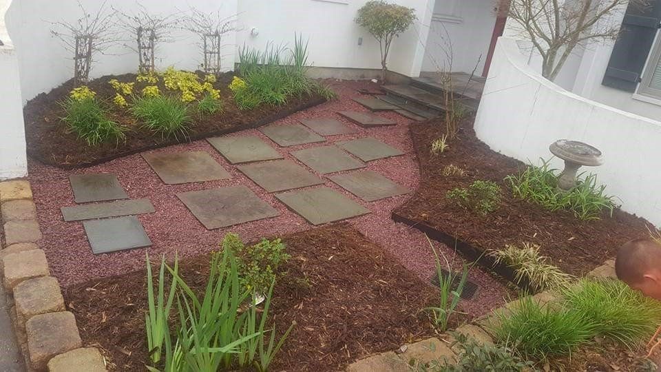 Garden bed with pink gravel, square stepping stones, and blooming spring flowers.
